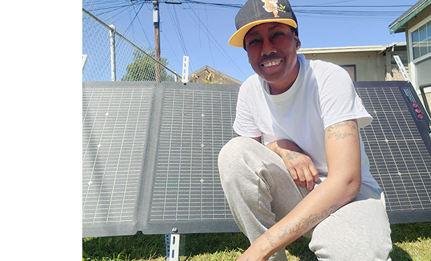 Sustainability grant recipient sitting in front of solar panels that he bought with a $1000 Intuit grant, smiling